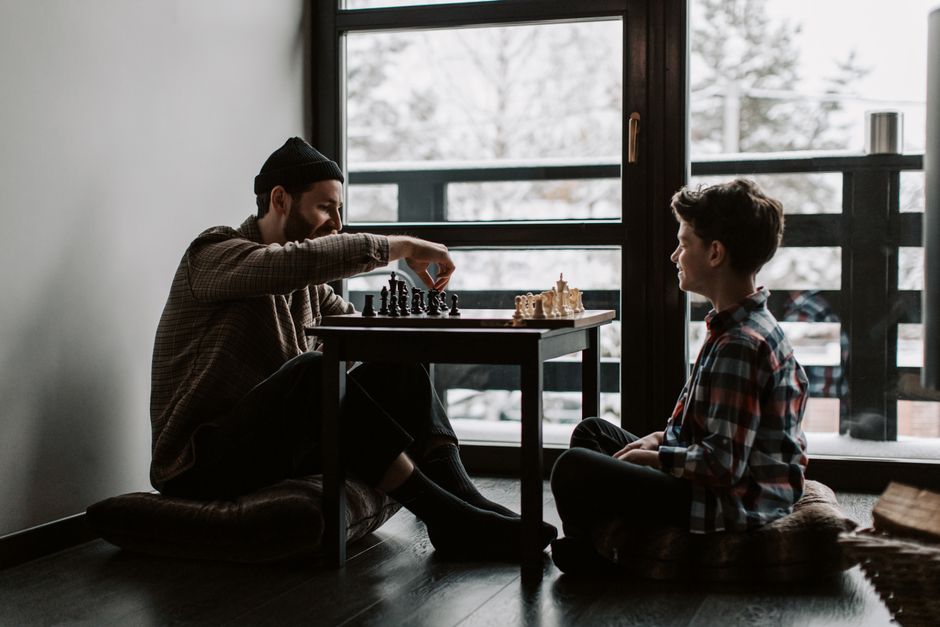 A man and boy playing chess indoors on a winter day, promoting family bonding.
