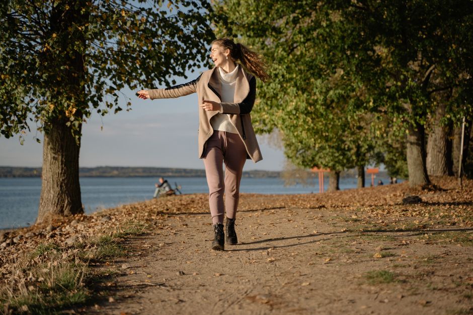 Woman enjoying a leisurely walk on a lakeside path in autumn with vibrant foliage.