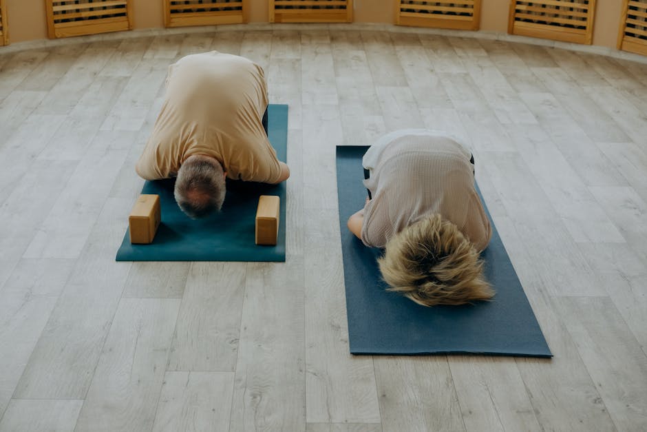 Senior couple doing yoga poses on mats in a calm indoor studio setting.