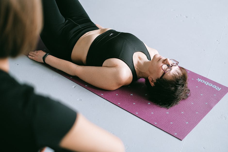 A woman wearing sportswear relaxing on a yoga mat indoors, reflecting calmness and fitness focus.