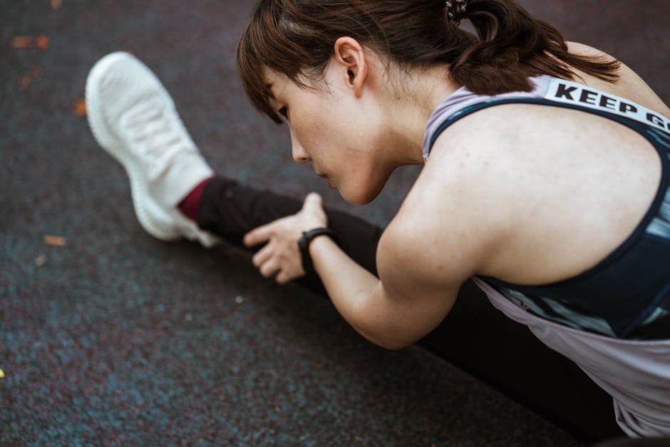 From above calm focused ethnic flexible female in sportswear warming up on sports ground