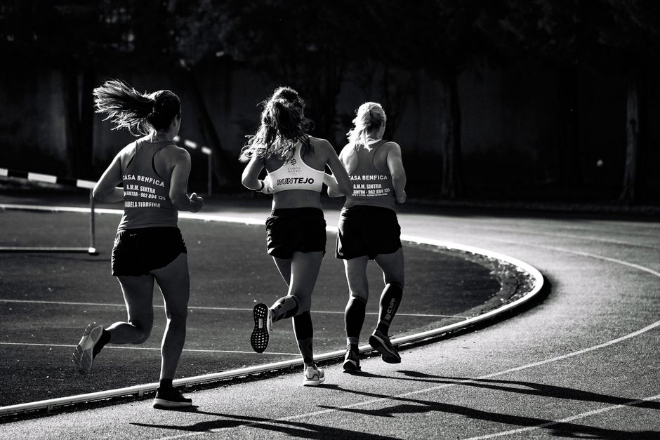 Black and white back view of unrecognizable fit female runners in sportswear running during track and field competition