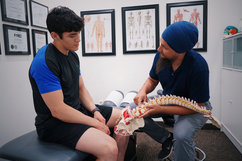 A doctor explains spinal issues to a patient using a spine model during a medical consultation.