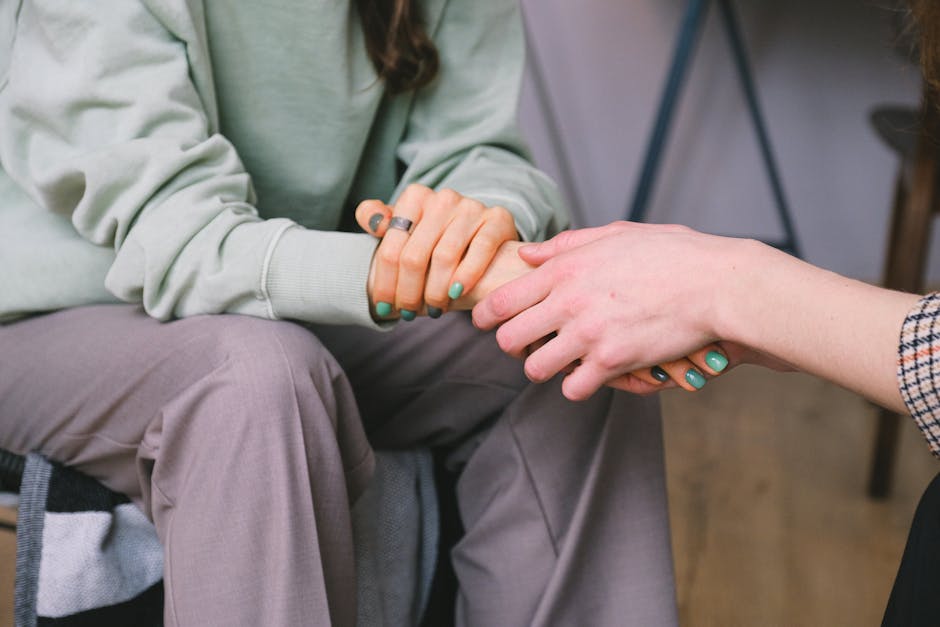 Crop unrecognizable counselor holding hand of woman while speaking during psychotherapy session and sitting in light workspace