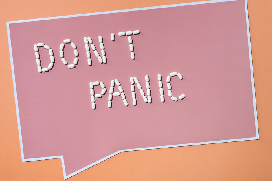 'Don't Panic' spelled with pills on pastel pink background, artistic and conceptual shot.