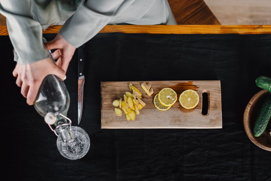 Top view of hands pouring water into a glass with lemon and ginger on a cutting board.
