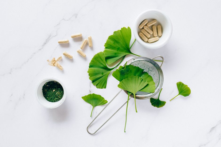 Flat lay of ginkgo leaves, capsules, and herbal powder on marble for natural health remedy.