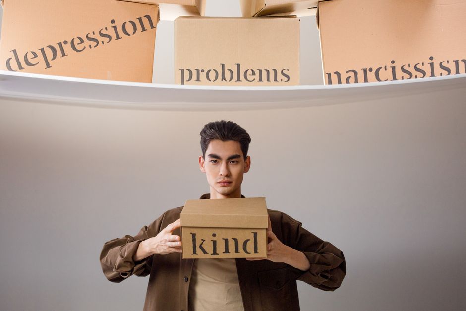 Creative image depicting a person balancing emotional concepts represented on cardboard boxes.
